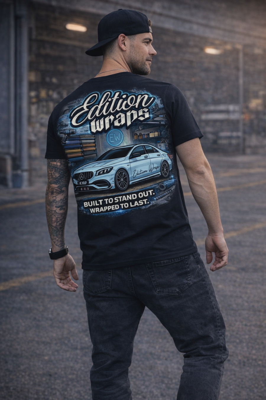 Man wearing a black t-shirt with a car graphic and text in an urban setting