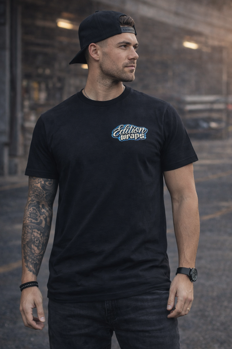 Man wearing a black t-shirt with a logo, standing in an urban setting.